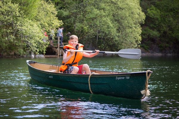 A child in an orange lifejacket paddling a green canoe